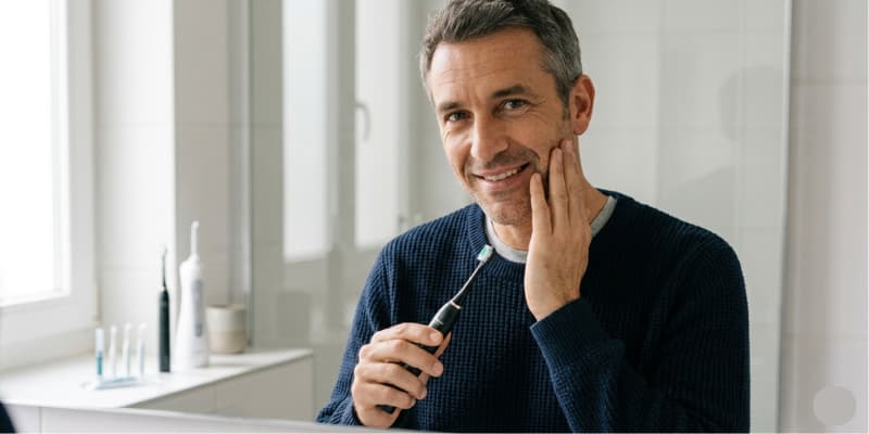 Homme de 45 ans utilisant une brosse à dents sonique Nomad avec tête Small Implant pour le nettoyage post-opératoire après une pose d'implant dentaire.